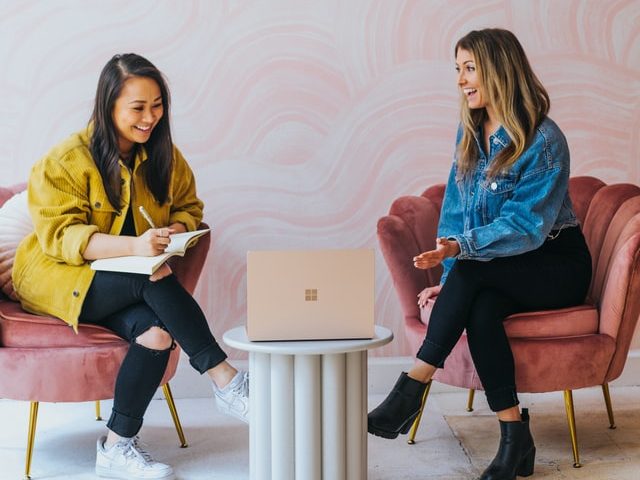 Two young women discussing marketing with laptop and notebook.